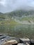 Vertical of a beautiful hiking destination with a shallow lake and green mountains captured in fog