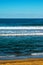 Vertical beautiful shot of wavy sea and sandy beach under blue sky