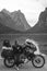 Vertical black and white photo. Girl motobiker in protective turtle jacket stands with touring motorcycle. Extreme vacation,