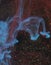 Vertical blue ink in water on black background with gold sparkles resembling a goat`s head nebula