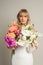 Vertical calm charming blond female bride in white dress with colorful flowers bouquet in studio. Wedding, engagement