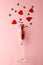 Vertical of champagne glass spilling red heart shapes on pale pink background with copy space