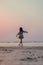 Vertical of a cinematic shot of a young woman walking in a beach in a pretty summer dress at sunset