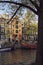Vertical cityscape shot of the Prinsengracht water canal with boats, green trees, traditional narrow Dutch houses with large