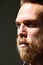 Vertical close-up of brutal man with ginger thick beard, looks thoughtfully aside, posing over black background.