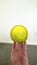 Vertical Close up of a hand holding a baseball against white wall and dark floor