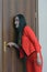 Vertical close-up portrait of a woman in a red suit eavesdropping, spying on the door of the boss