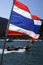 Vertical close up shot of the flag of the Kingdom of Thailand waving in the wind with a blurred wooden fisherman boat, dark blue