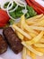 Vertical close-up shot of French fries, kebabs and vegetables on a plate