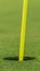 Vertical Close up view of the yellow pin and cup of a golf course on a sunny day