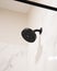 Vertical closeup of a black showerhead in a bathroom with marble tiles