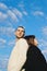 Vertical closeup of a couple standing their backs close sunlit cloudy sky background