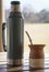 Vertical closeup of a cup of yerba mate infusion with a thermos.