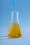 Vertical closeup of dropper with blue liquid over Erlenmeyer flask yellow liquid on blue background