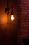 Vertical closeup of a lamp indoors with metallic diamond form covering, brown brick wall background