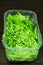 Vertical closeup shot of arugula in a plastic bowl on a wooden surface