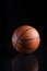 Vertical closeup shot of a brown basketball ball with lines on a black background with a reflection
