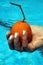 Vertical closeup shot of a female hand holding a wrinkled orange a swimming pool