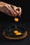 Vertical closeup shot of hands cracking an egg, yolk and white falling onto the pan