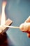 Vertical closeup shot of a person lighting a match on a matchbox on a blue background