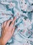Vertical closeup shot of a person\'s hand on blue bedsheets with flowers