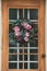 Vertical closeup shot of a wooden and glass door with pink roses hanging on it