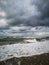 Vertical closeup of a stormy sea making foam on the beach, gloomy, cloudy sky background