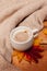 Vertical cozy picture of Breakfast, coffee with milk foam in a white mug, autumn red and yellow maple leaves and a knitted beige