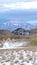 Vertical crop Snowy hilly terrain with houses against sunlit frosted mountain in winter