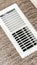 Vertical crop White air conditioner duct grille cover against floor with brown carpet