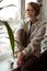 Vertical dreaming, tranquil, thoughtful blond woman in glasses and warm sweater sitting on windowsill with coffee mug