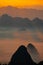 Vertical drone shot of silhouettes of green-covered hills in mist at sunset, cool for background