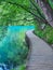 VERTICAL: Empty walkway runs along the shore of emerald lake in Plitvice park.