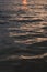 Vertical filled frame full screen desktop wallpaper shot of evening calm sea at dusk with orange sun reflection that makes the