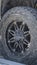 Vertical frame Black rubber wheel of a silver vehicle parked on the road on a sunny day