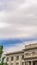 Vertical frame Building with white wall balcony and security camera on roof against cloudy sky