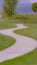 Vertical frame Curvy pathway small pond bench and trees on a grassy terrain under cloudy sky