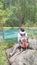 The vertical frame. A female brunette traveler is sitting on the edge of a beautiful turquoise lake. A backpack, sweatshirt. Hike