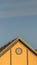 Vertical frame House exterior with roof shingles and round gable window against blue sky