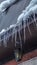 Vertical frame Spiked icicles at the edge of pitched gray roof with clumps of snow in winter