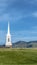 Vertical frame White steeple and rooftop of a church viewed from a grassy hill on a sunny day