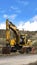 Vertical frame Yellow excavator and orange traffic delineator post beside a mountain road