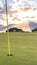 Vertical frame Yellow flagstick and hole at a golf course against lake mountain and cloudy sky