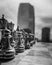 Vertical grayscale shot of chess figurines with buildings in the background in Denver