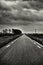 Vertical grayscale shot of a highway in a rural area under the dark cloudy sky