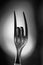 Vertical greyscale shot of a bent metal fork symbolizing the sign of rock music