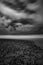 Vertical greyscale shot of pebbles on the body of the sea under the dark cloudy sky