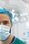 Vertical half portrait of caucasian male surgeon in surgical mask and cap in operating theatre