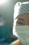 Vertical half portrait of smiling asian female surgeon in surgical cap and mask, with copy space