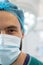 Vertical half portrait of smiling caucasian male surgeon in surgical mask and cap in theatre